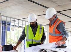 two people wearing hard hats and vests looing at paper