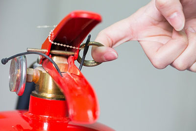 close-up of finger pulling pin on fire extinguisher