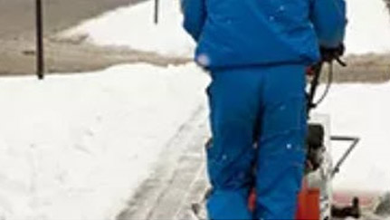 person pushing snow blower on snow-covered sidewalk